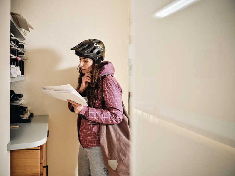 Eine Frau mit Fahrradhelm ist gerade im Büro angekommen und öffnet Post