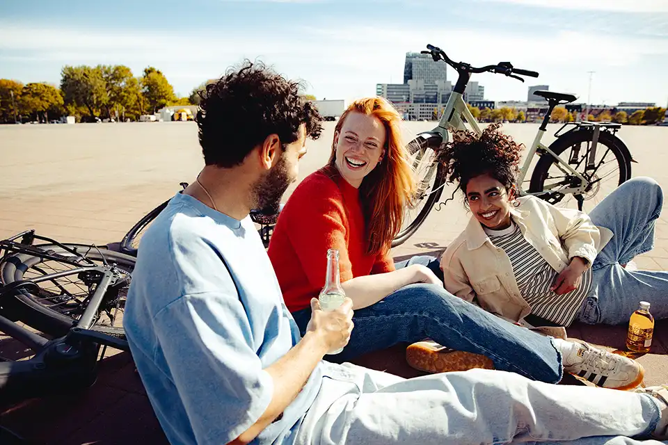 Gruppe junger Menschen mit ihren Fahrrädern auf einem urbanen Platz trinken Limo