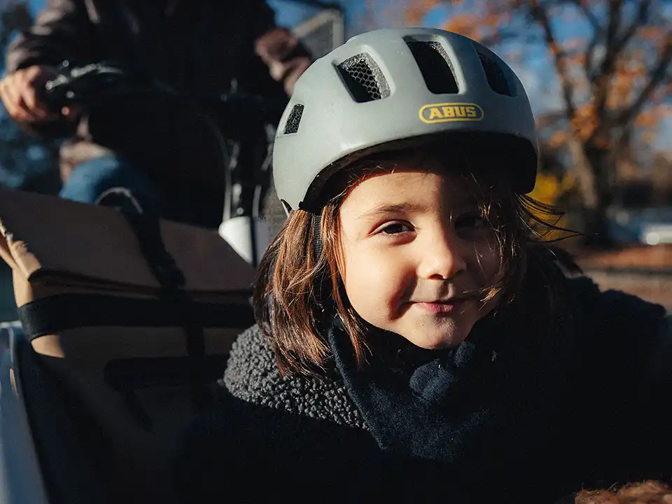 Mädchen mit Fahrradhelm sitzt im Lastenrad und schaut dich an. Ihr Gesichtsausdruck zeigt: Sie weiß Bescheid.