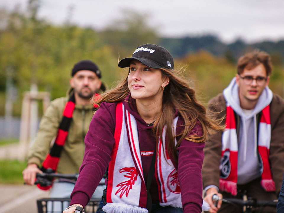 Fans radeln zum Stadion mit Fanschals des SC Freiburg um den Hals